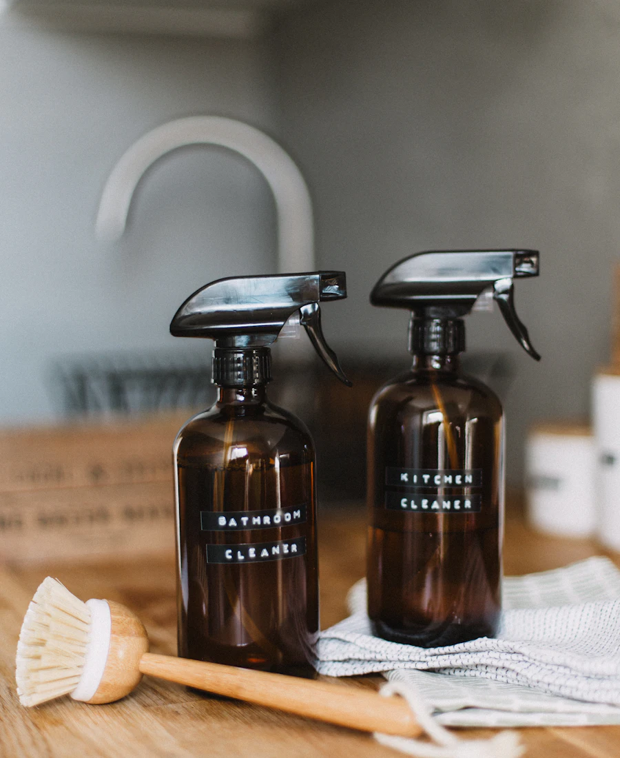Amber glass spray bottles and a natural bristle brush on a wooden counter